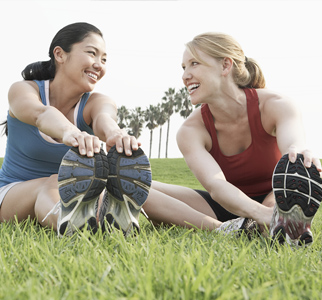 2 teen girls sitting on the ground, stretching their hamstrings