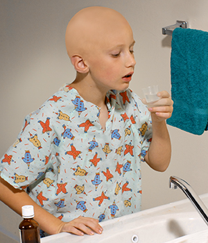 Child standing at bathroom sink preparing to rinse mouth. Bottle of rinse is on counter next to sink.