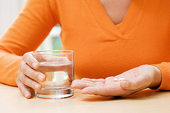 Close view of a owman's hannds. One is holing two pills and the other holds a glass of water.