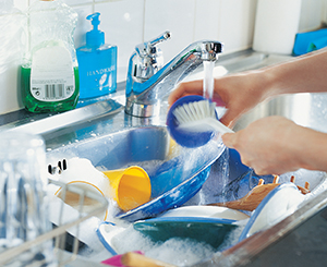 Manos con guantes de goma en el fregadero de la cocina, lavando un plato con agua y jabón.