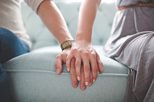 Closeup of man and woman holding hands while sitting on a couch.