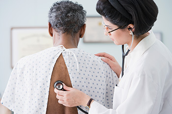 Doctor pressing stethoscope to man's back and listening
