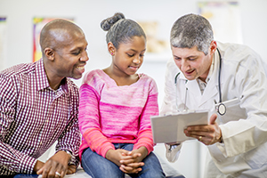Doctor reviewing chart with young girl patient and her father.