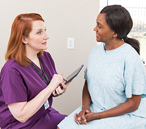 Woman wearing hospital gown speaking to healthcare provider.