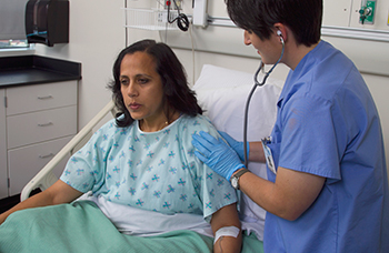 Health care provider listening to the lungs of a woman in hospital bed.