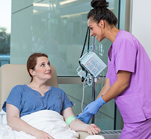 Healthcare provider caring for woman having infusion treatment.