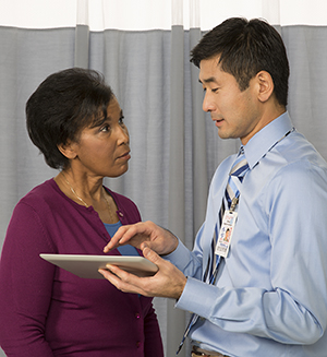 Healthcare provider holding electronic tablet, talking to woman.