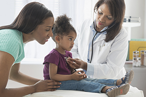 Healthcare provider listening to girl's chest with stethoscope.