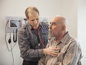 Healthcare provider listening to man's chest with stethoscope.