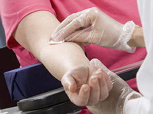Healthcare provider preparing woman's arm for blood draw.