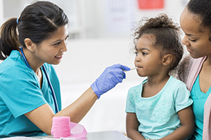 Girl sitting on mother's lap while healthcare provider takes her temperature.