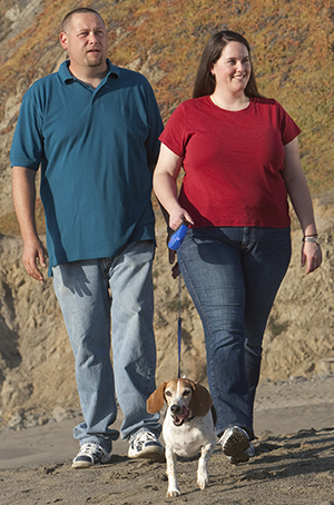 Man and woman walking dog on the beach.