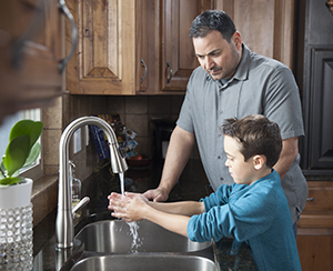 Man helping boy wash hands in kitchen sink.