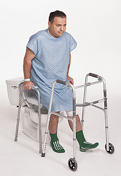 Man in hospital gown in bathroom holding onto toilet side rails to help steady him while he sits on toilet.