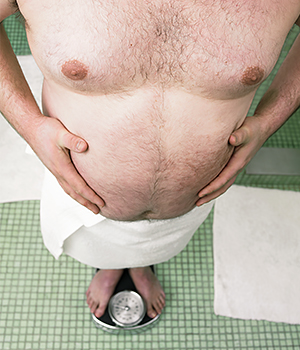 Man in the bathroom, wearing a towel, weighing himself.