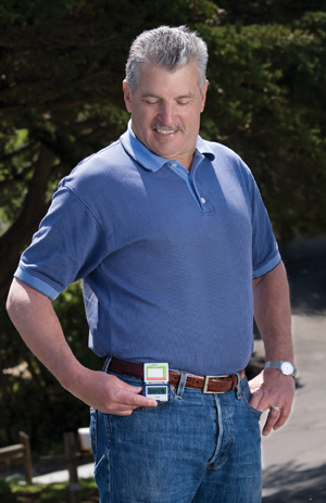 Man outside looking at pedometer on his belt.