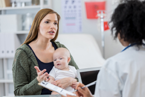 Mother holding a baby boy talking to a female healthcare provider.