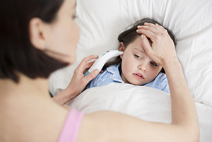 Mother taking daughter's temperature in bed.