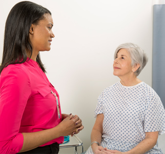 Older woman in hospital gown talking with her doctor