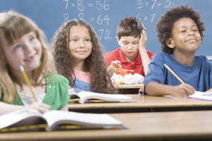 One boy in back of classroom looking down at crumpled paper on his desk distracted from the class.