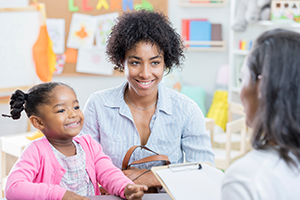 Parent with child speaking to teacher in classroom.