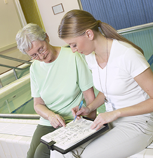 Physical therapist sitting with senior woman looking at exercise sheet.