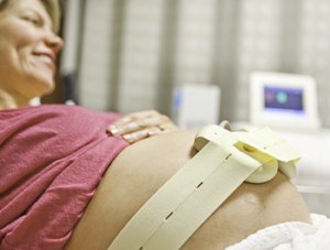 Pregnant woman lying on exam table with straps around belly. Straps are connected to machine.