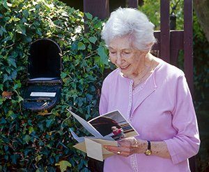 Senior woman standing at mailbox in front of house.