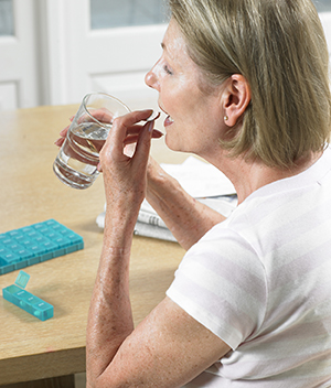 Senior woman taking pill with water.