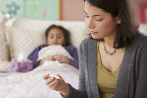 Woman checking thermometer and a sick child resting in bed.