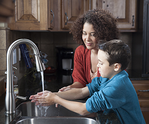 Woman helping boy wash hands in kitchen sink.