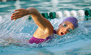 Woman lap swimming in pool wearing goggles and swim cap.