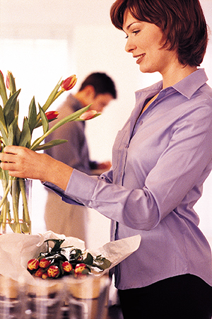 Woman placing flowers in vase with husband in the background.