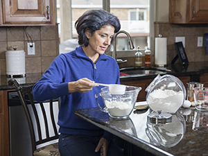 Woman sitting at kitchen counter, measuring baking ingredients.