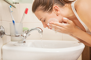 Woman washing face over sink.