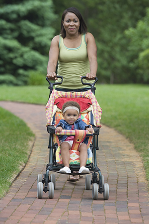 Young mother walking with baby carriage in park.