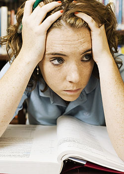 Young woman studying and looking stressed. She's holding her head and hair in her hands.