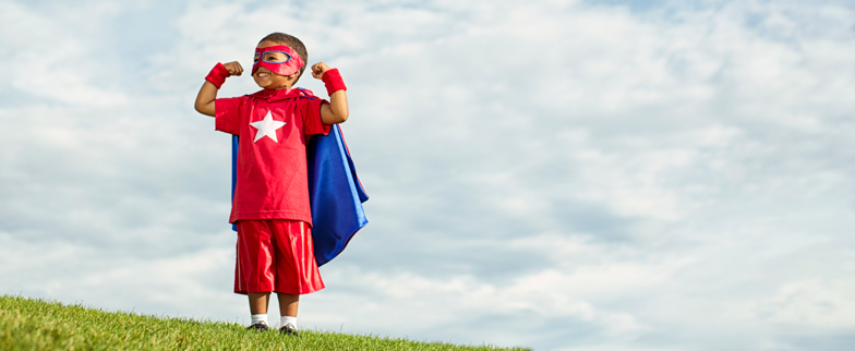 Little boy wearing a superhero costume outside in a superhero stance