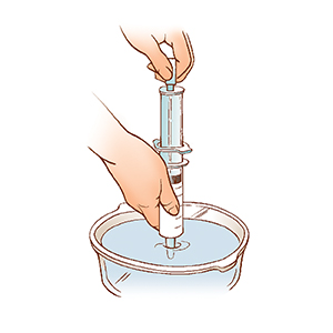 Closeup of hands holding syringe with tip in bowl of water, pulling plunger to draw water into syringe.