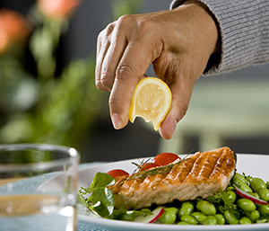 Closeup of man's hand squeezing lemon on broiled salmon.