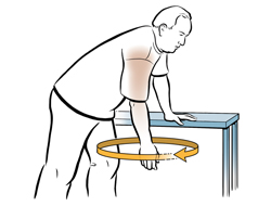Man bending forward with one hand on table for support,  swinging other arm in circle doing shoulder exercise.