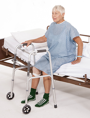 Woman sitting on edge of hospital bed with walker.