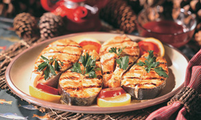 Grilled salmon steaks on a plate with lemon and tomato slices.