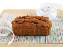 Pumpkin cranberry gift loaf sitting on wrapping paper with a piece of ribbon sitting next to it.