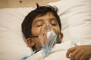Boy resting in a hospital bed with an oxygen mask.