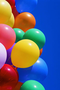 A cluster of colorful balloons agains a blue sky.
